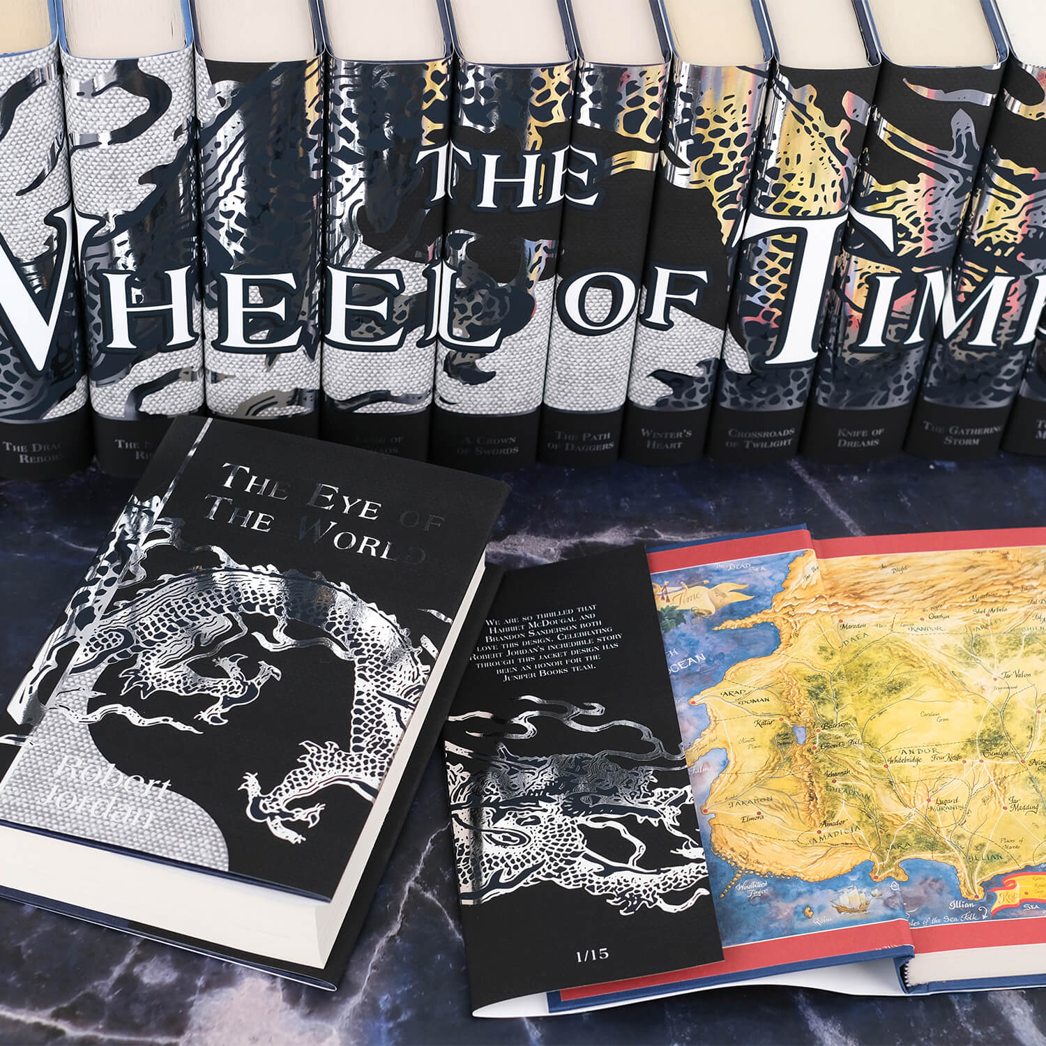 Open book view of New Spring set against the other books in the series by Robert Jordan. Open book displays flap text on the inner front flap. The covers feature a silver foil dragon traveling across the front onto the inner flap. Book titles and the author's name on the front cover are in silver foil. All three books sit on a blue marble background.