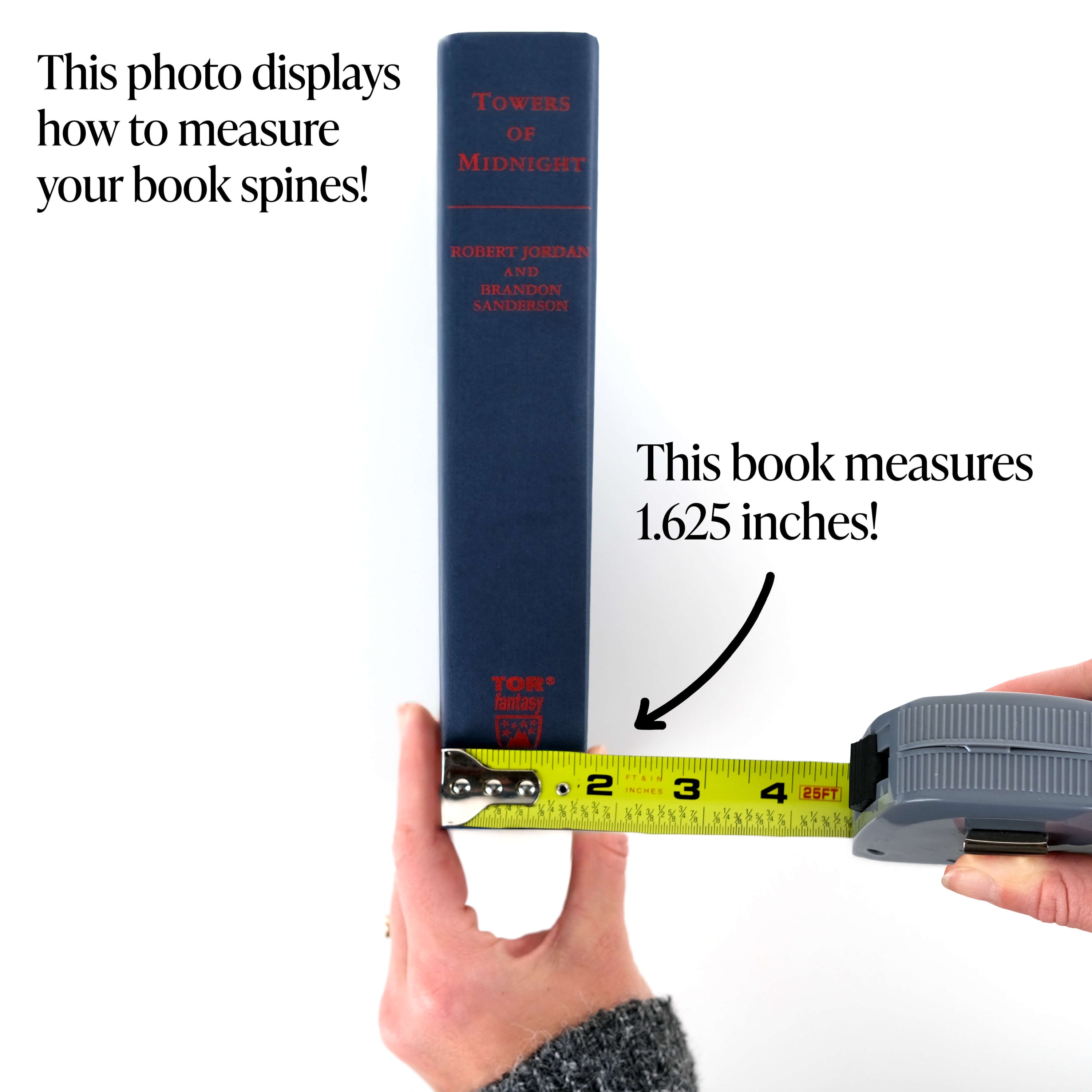A hand holding an unjacketed Towers of Midnight book spine up against a white background. The other hand holds a tape measure against the spine measuring the width showing how to measure your books.