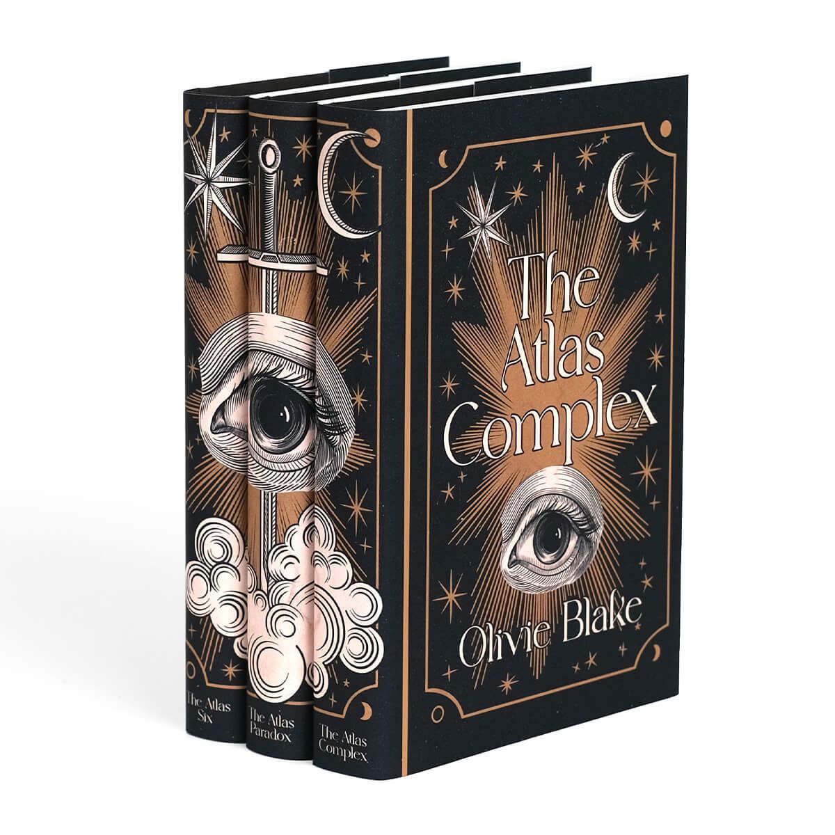 Angle shot of The Atlas Series by Olivia Blake. Front covers of jackets feature woodcut eye illustration between book title and author name surrounded by cooper colored stars and ornamental detailing.
