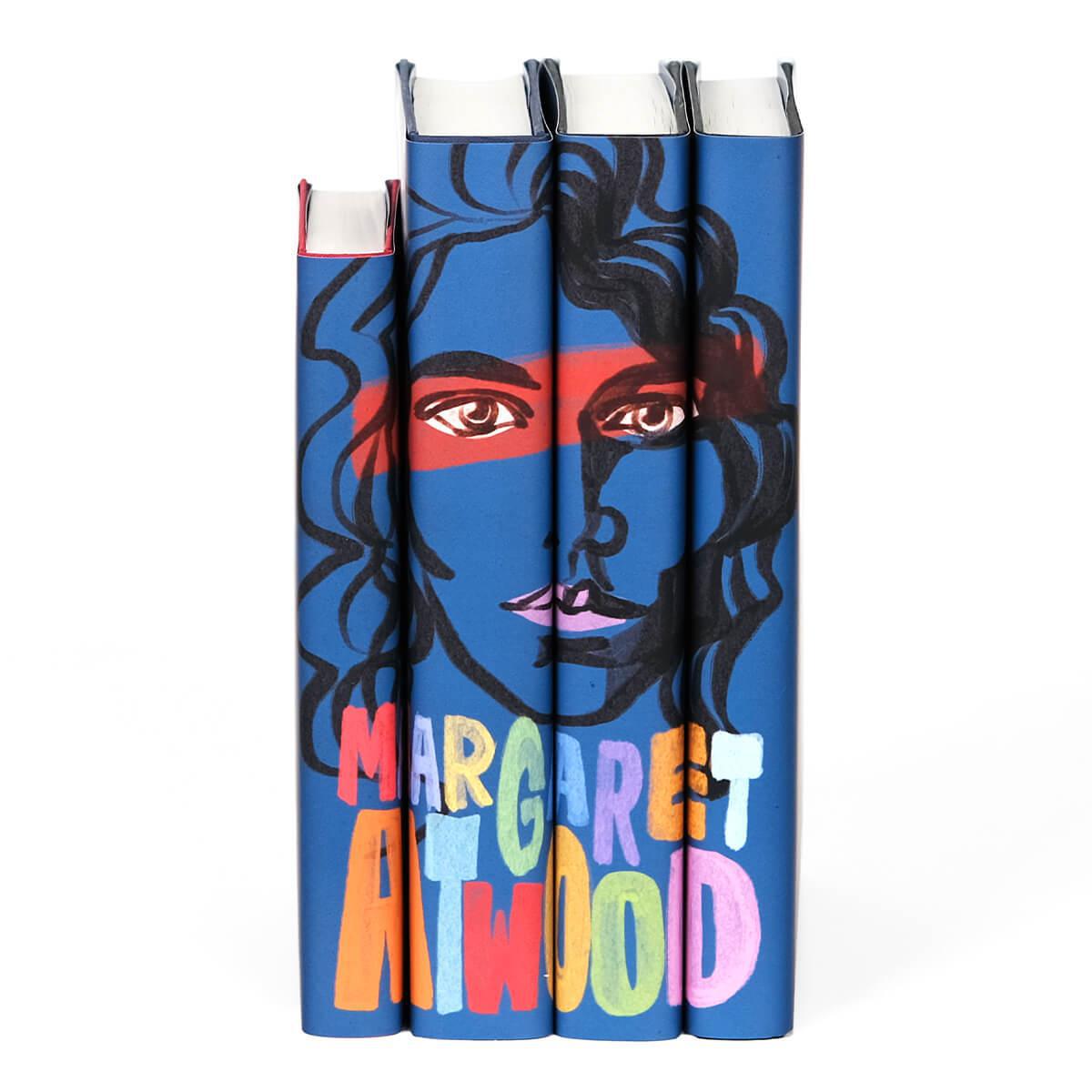 Front image of Margaret Atwood book set from Juniper Books. Deep blue dust covers featuring a sketch illustration of Margaret across the spines with her name below portrait in rainbow block letters.