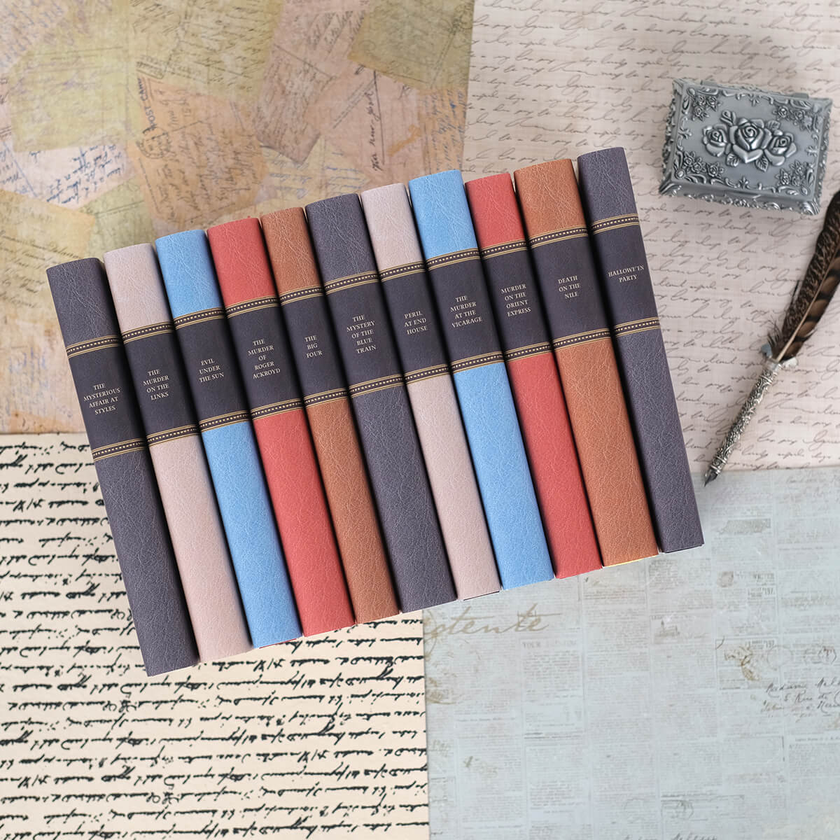 Agatha Christie books wrapped in custom collectible faux leather dust jackets sit against background of cursive letter and newsprint.. Book spines feature book titles typed in gold color serif font set against back faux leather.