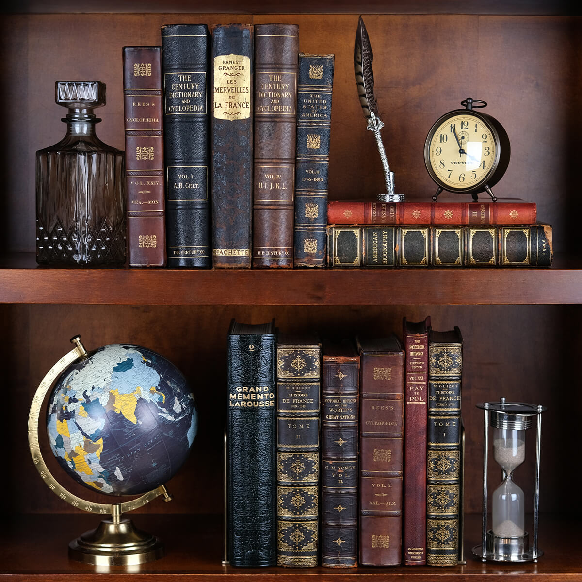 This image features a bookshelf filled with antique leather-bound books with gold embossing, exuding vintage elegance. The collection includes encyclopedias, dictionaries, and historical volumes in French and English, such as "Grand Mémento Larousse." The aged spines, intricate detailing, and rich patina highlight their historical value. Complementing the books are vintage decor pieces like a globe, an hourglass, and a quill pen, enhancing the classic library aesthetic.