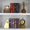 Install shot of all 12 BESO book covers from Juniper Custom on a white bookshelf surrounded by antique leather books, a clock, a bookend, and dried flowers.