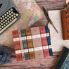 A styled flat-lay featuring a collection of seven Nobel Laureate books with gradient-toned dust jackets arranged neatly on a rustic wooden surface. Surrounding elements include a vintage typewriter, a map, a feather quill on handwritten parchment, marbled book covers, and lavender sprigs, creating a literary and nostalgic atmosphere.