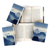 A collection of women authors with blue atmospheric watercolor mountain book covers. The books are arranged on a white background, with one book open to display text size. The front covers have book title.