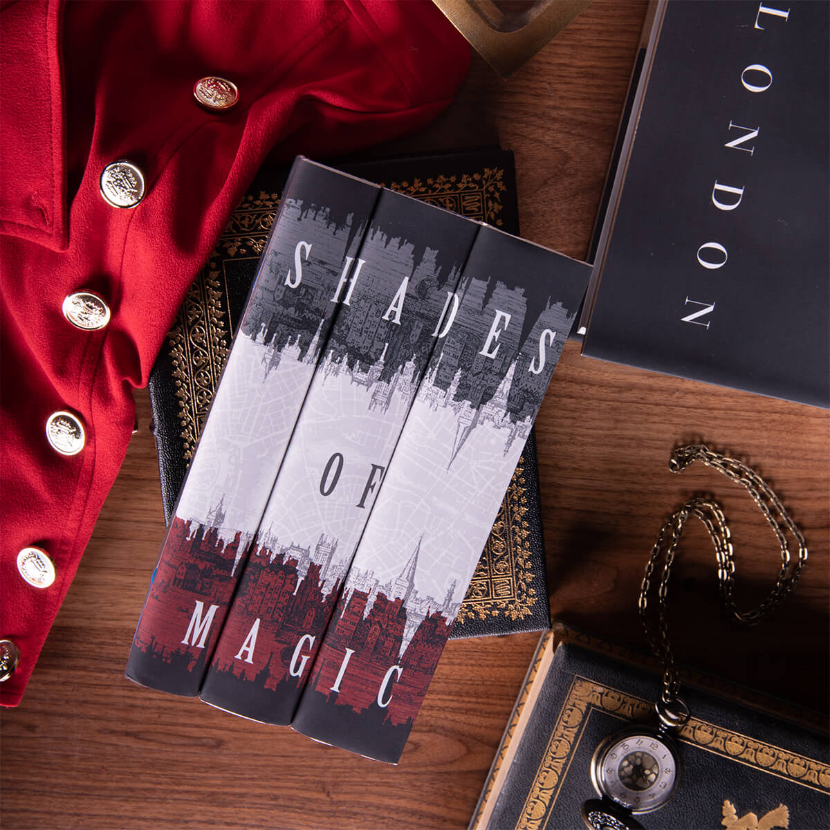 Flat lay of Shades of Magic set from Juniper Custom. Set sits on antique leather books surrounded by a red coat, book on London, and a pocket watch set against wood background.