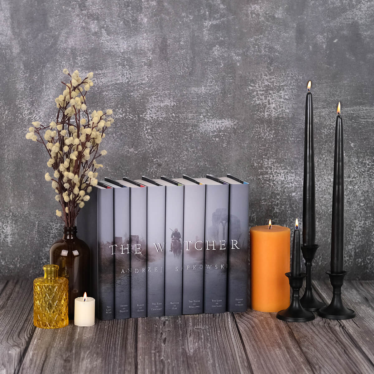 Install shot of the Witcher book set from Juniper Custom. Book set sits against grey stone background surrounded by lit candles and glass bottles.
