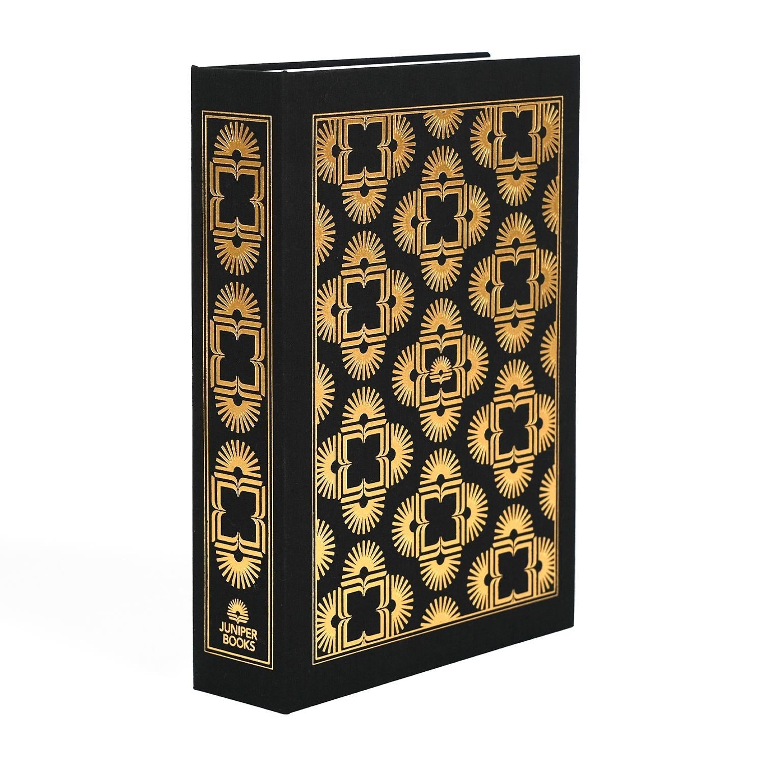 The black dust jacket box by Juniper Books, resembling a hardcover book spines. The box features intricate, symmetrical patterns in metallic colors on the spine and covers—gold on a black box. The Juniper Books logo is displayed at the bottom of each spine.