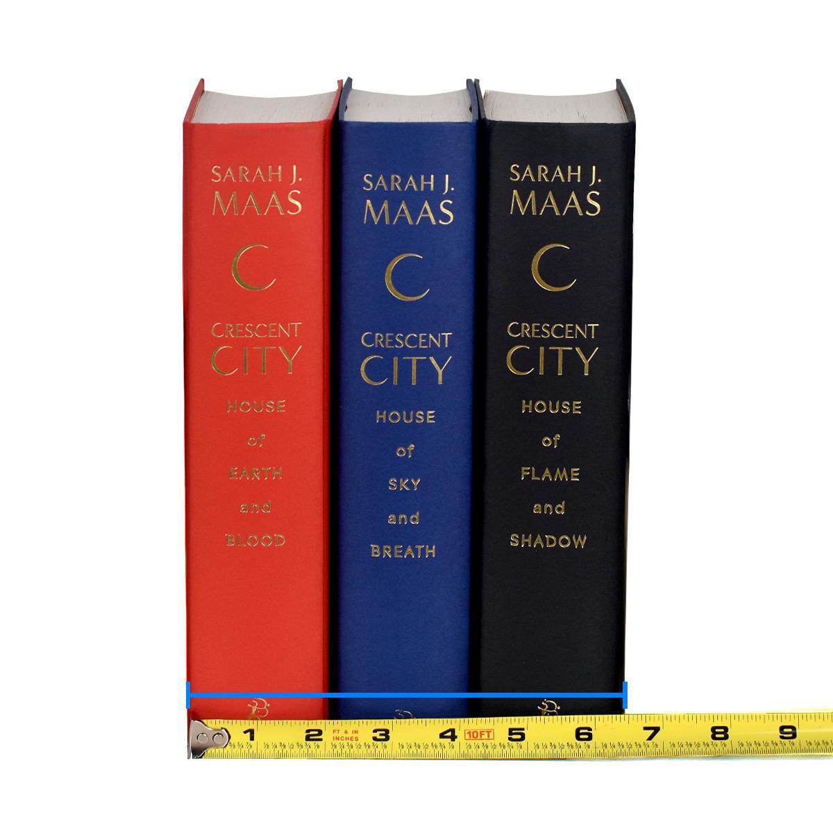 Unjacketed photo of three books in Crescent City Series by Sarah J. Maas. Books are red, blue, and black with gold type down the spine detailing author name and book title. Tape Measure rests against bottom displaying width of set.